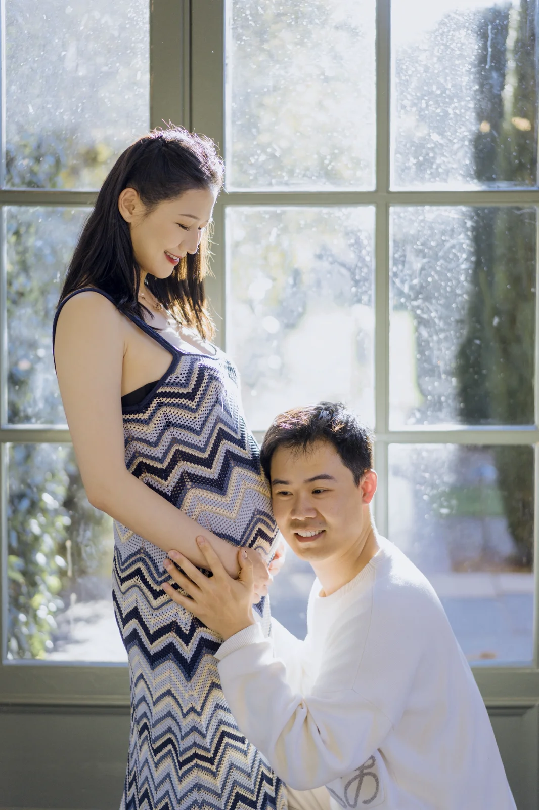 Expecting couple embracing in a sunlit field during an outdoor maternity session.